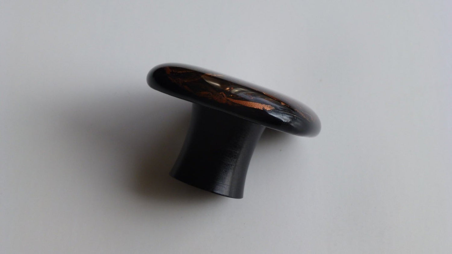 A copper knob on it's side, showing the satin black aluminum base. Made in USA. Ann Ivory Studios.